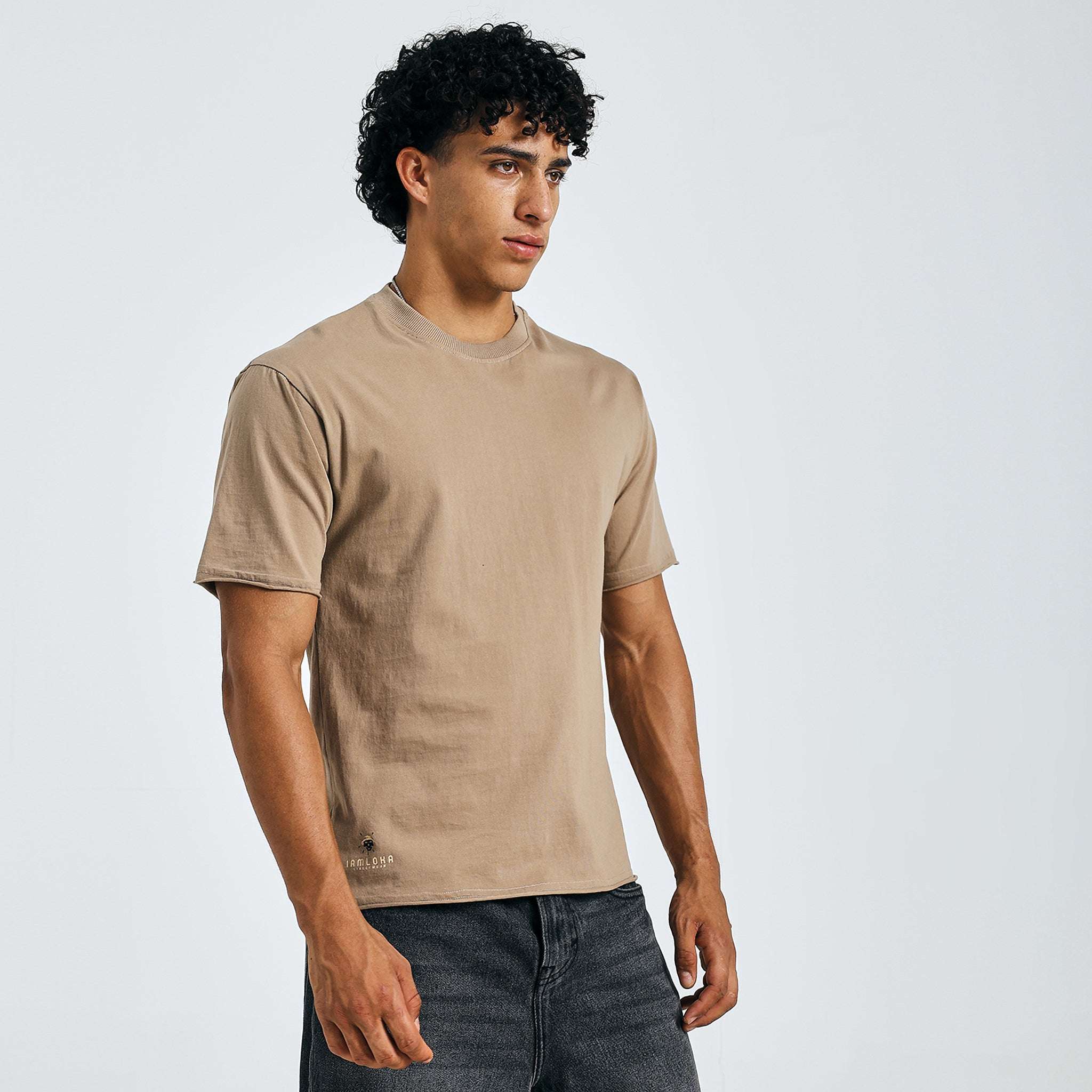 Buy beige minimalist graphic tee, fashion pose with sunglasses, paired with jeans.