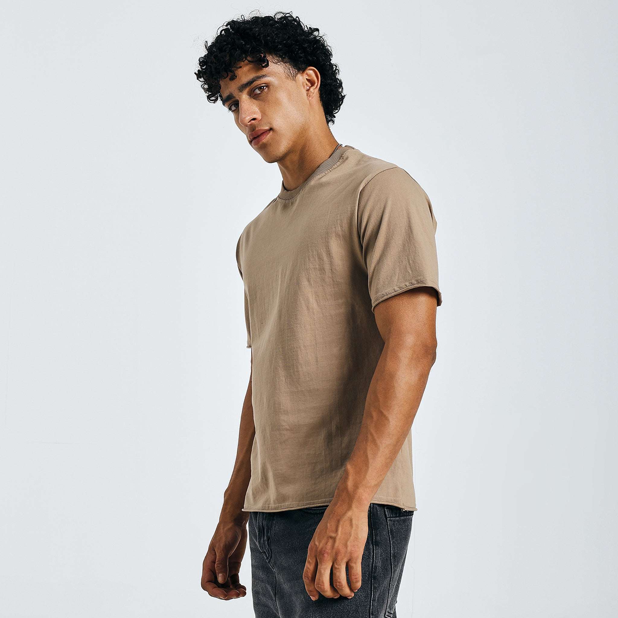 Beige minimalist graphic tee, side view, with black jeans on model.