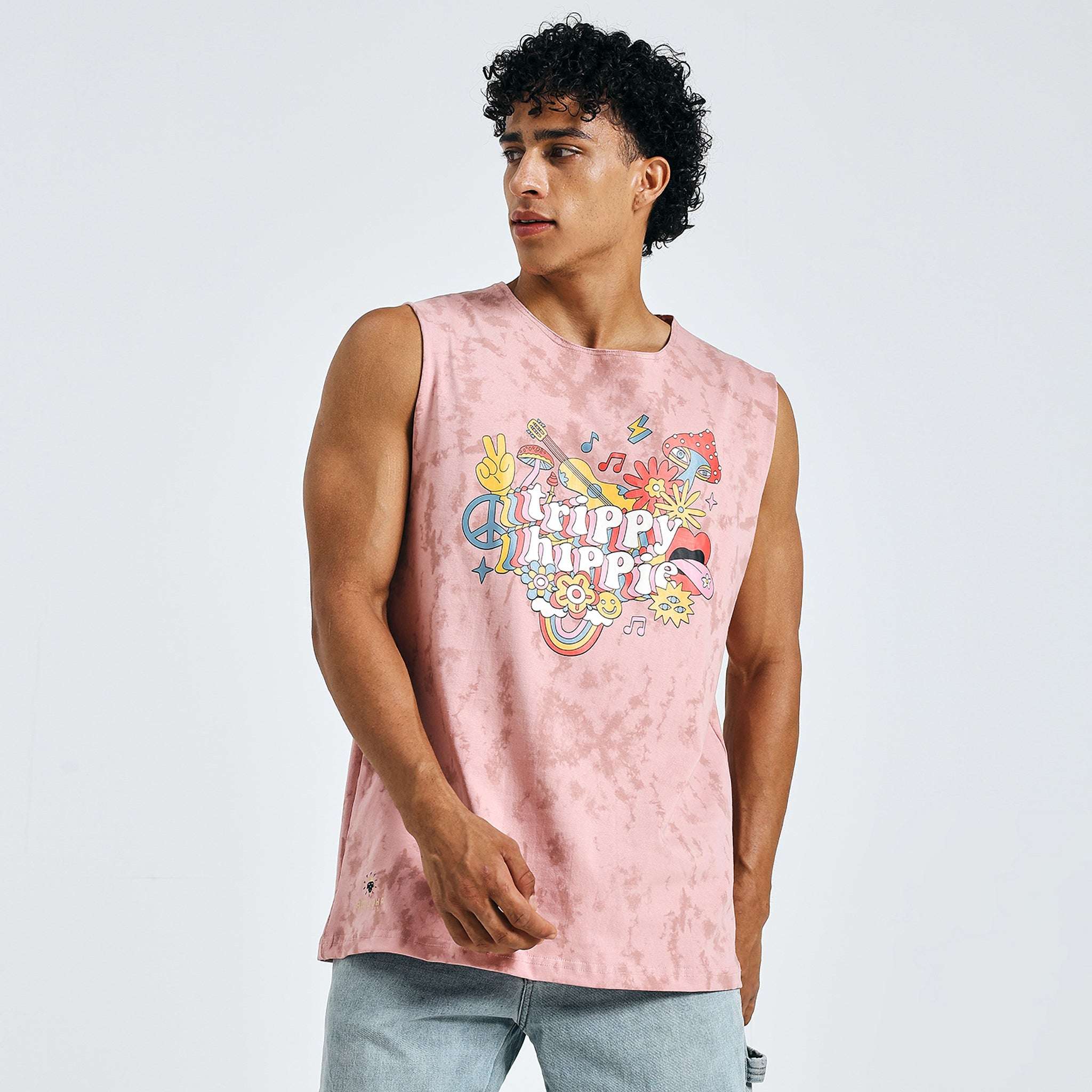 Front view of man wearing pink sleeveless “Trippy Hippie” graphic t-shirt with light denim shorts