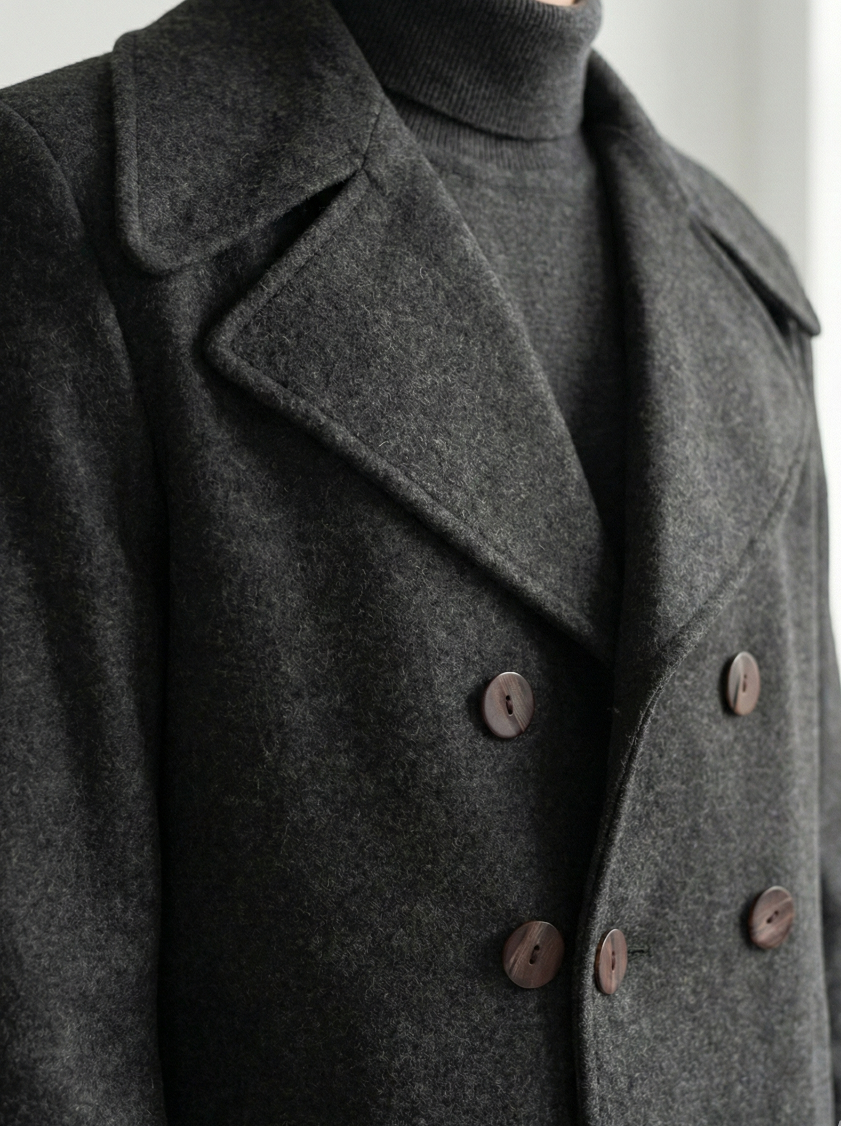 Close-up of a dark gray peacoat with brown buttons on a neutral background