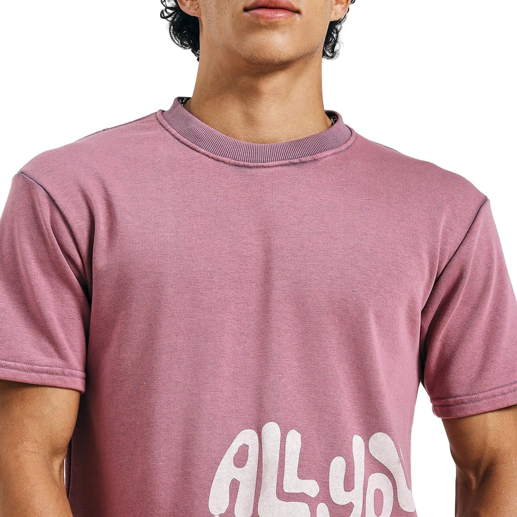 Person wearing a pink t-shirt with 'ALL' printed on it against a white background