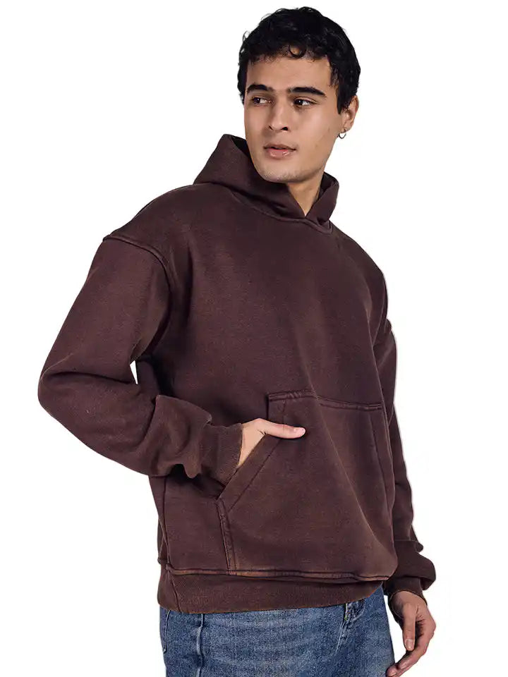 Man wearing a brown acid wash hoodie and blue jeans on a white background