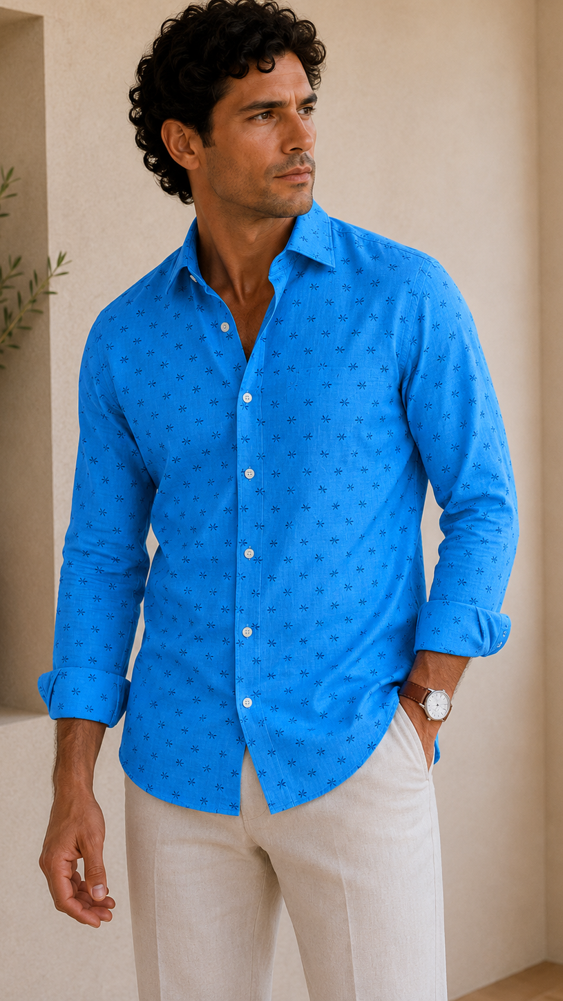 Man wearing a blue patterned shirt and beige pants standing indoors.