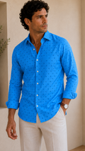 Man wearing a blue patterned shirt and beige pants standing indoors.