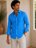 Man wearing a blue patterned shirt and beige pants standing indoors.