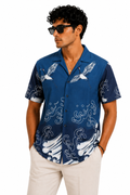 Man wearing a blue patterned shirt with white pants on a white background