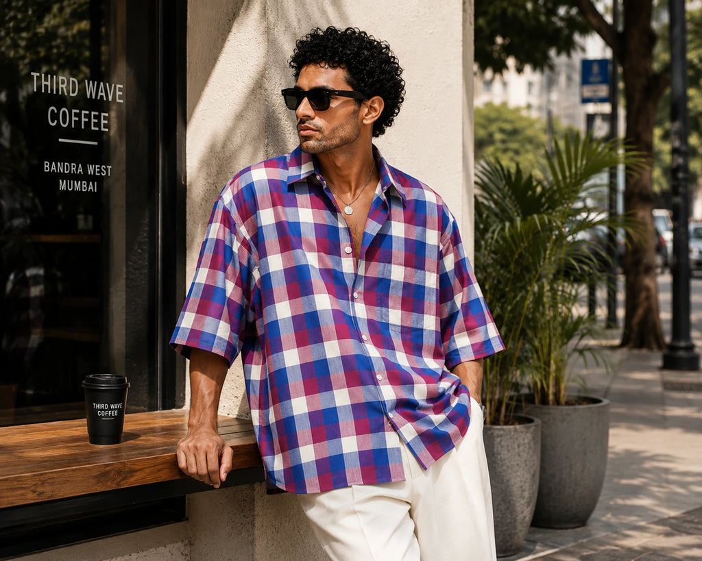Man wearing a plaid shirt standing outdoors near a coffee shop.