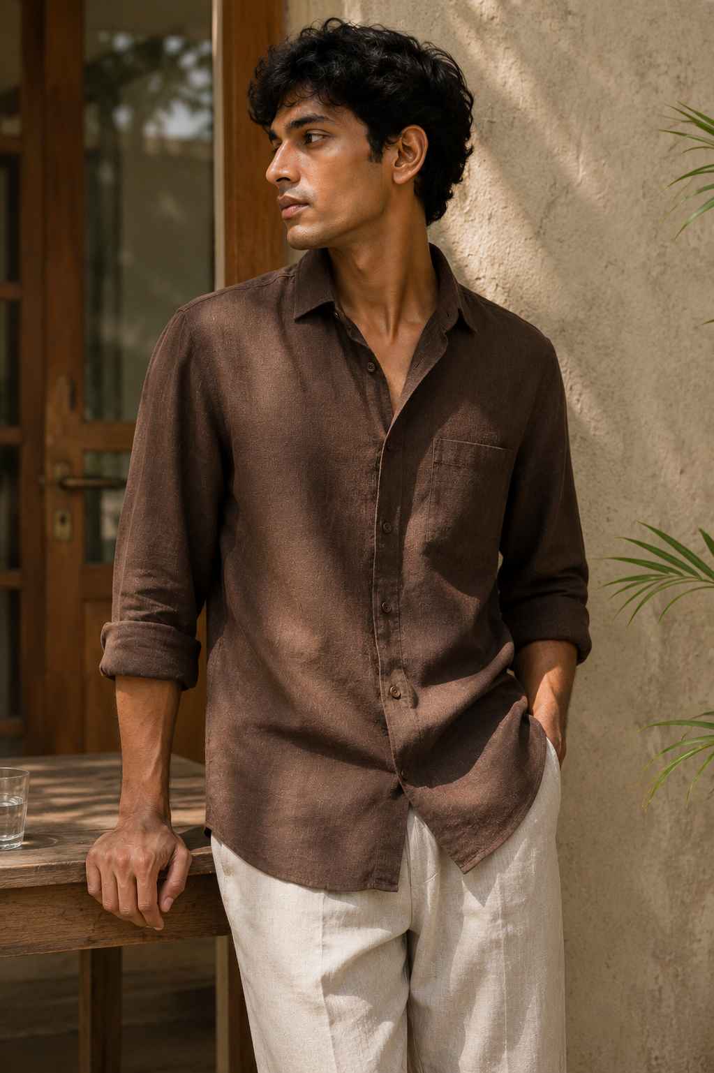 Man wearing a brown shirt and white pants leaning against a wall.