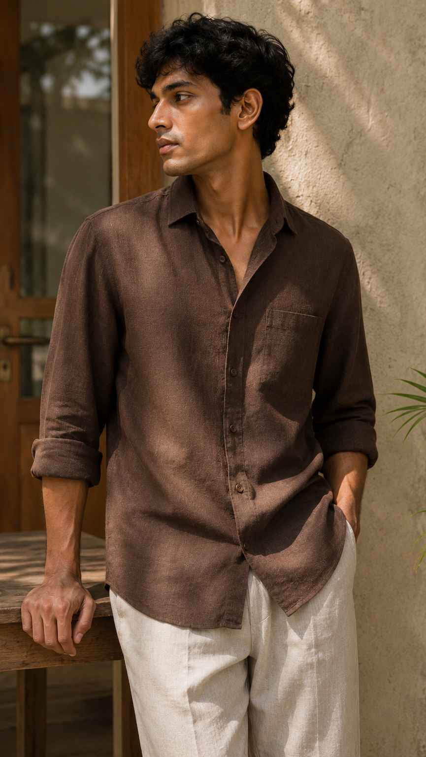 Man wearing a brown shirt and white pants leaning against a wall.