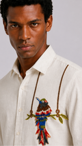 Man wearing a white shirt with a colorful embroidered parrot design on a gray background