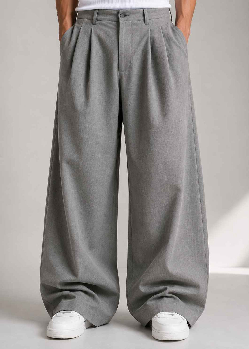 A person wearing wide-leg gray pleated trousers with a white top and white sneakers, shown from the waist down against a light gray studio background.