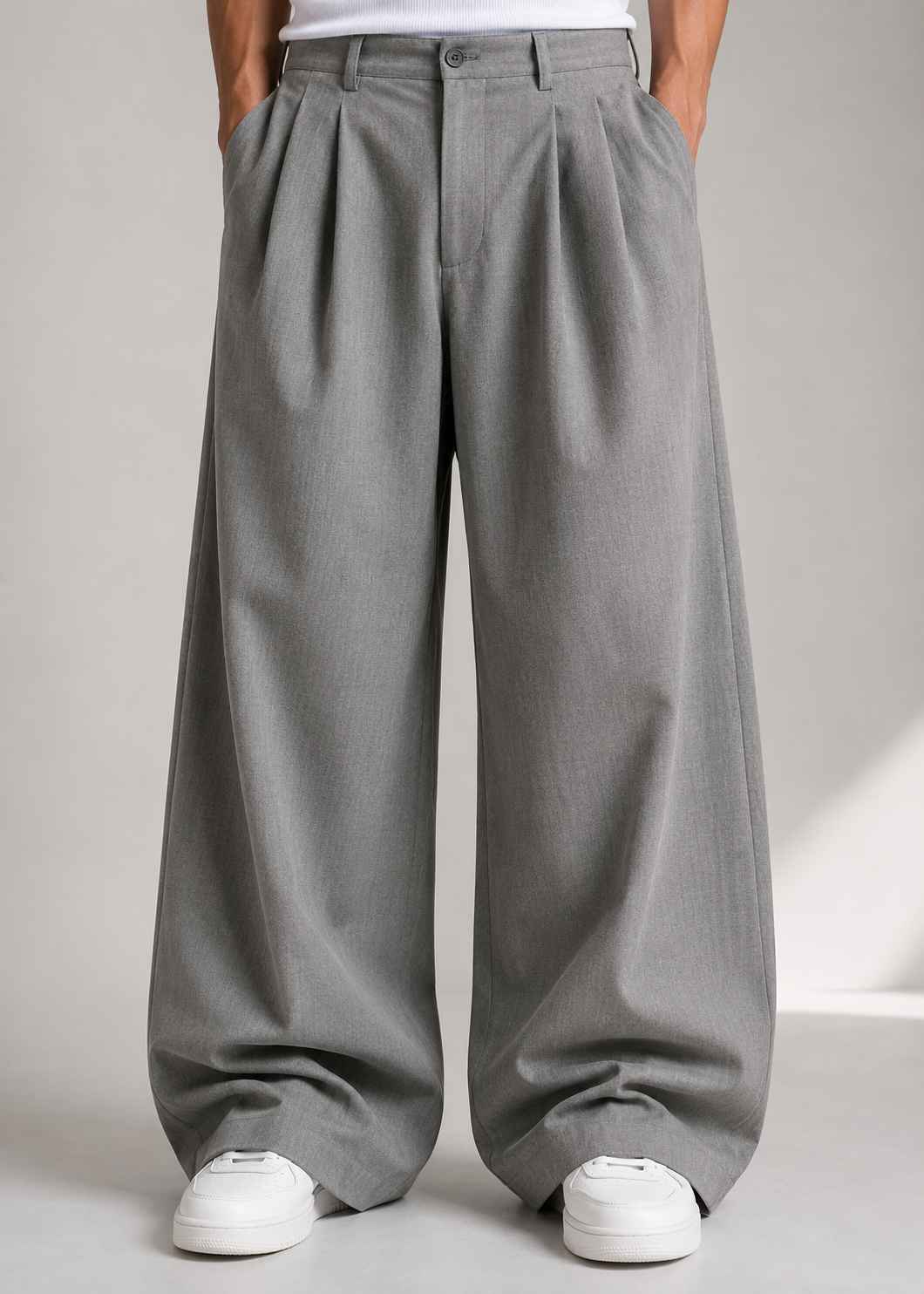 A person wearing wide-leg gray pleated trousers with a white top and white sneakers, shown from the waist down against a light gray studio background.