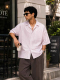 Man in a striped shirt and sunglasses holding a coffee cup, standing on a street.