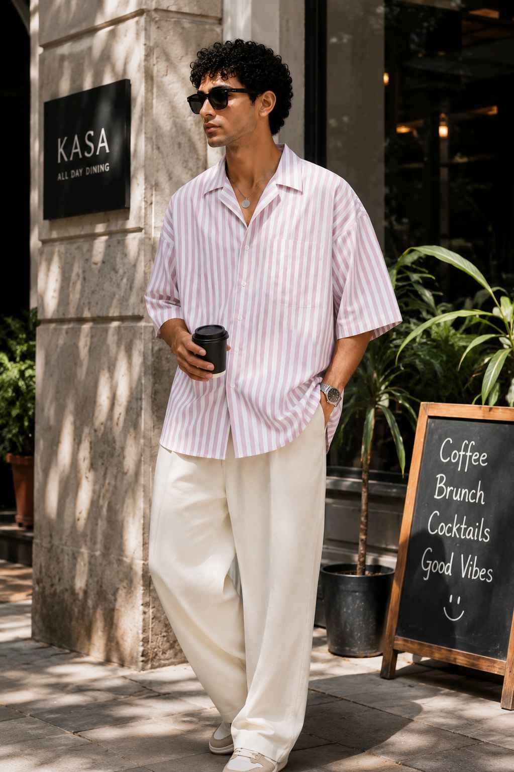 Man holding a coffee cup standing outside a building with 'KASA' sign.