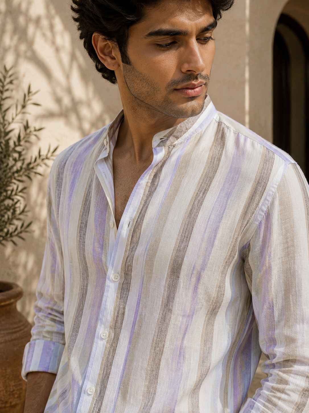 Man wearing a striped shirt outdoors with plants in the background