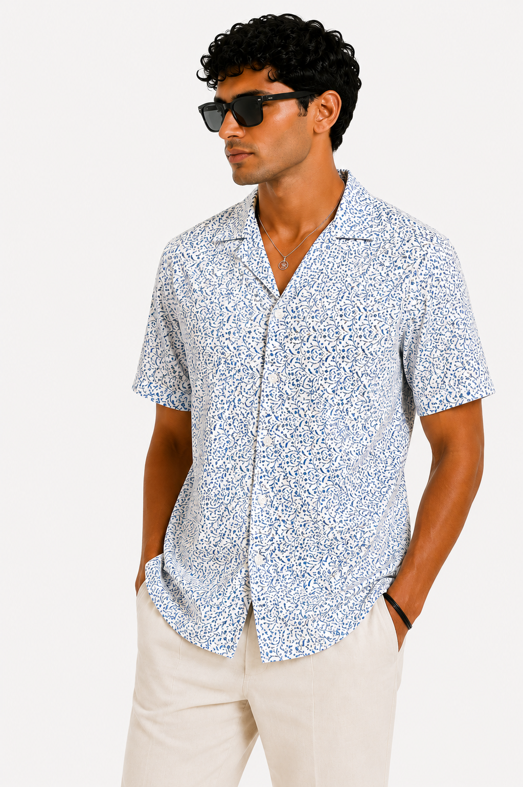 Man wearing a patterned short-sleeve shirt and sunglasses on a white background
