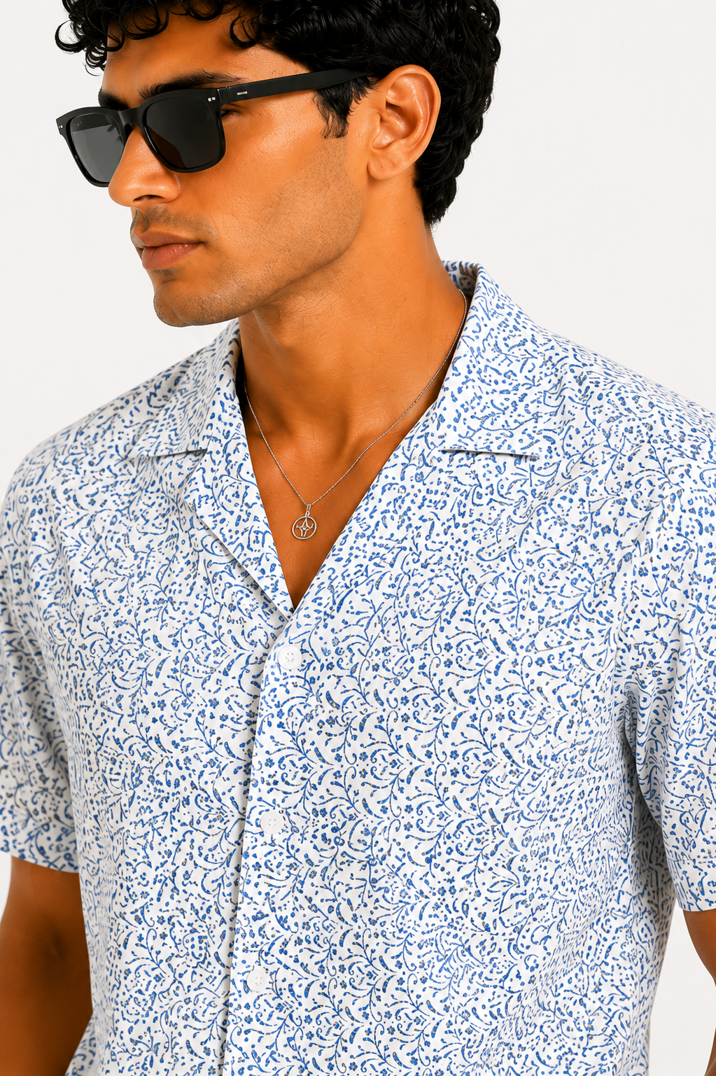 Man wearing a patterned shirt and sunglasses against a white background