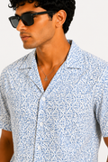 Man wearing a patterned shirt and sunglasses against a white background