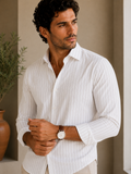 Man wearing a white striped shirt with a watch, standing indoors.