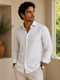 Man wearing a white striped shirt standing in a room with a window and plant.