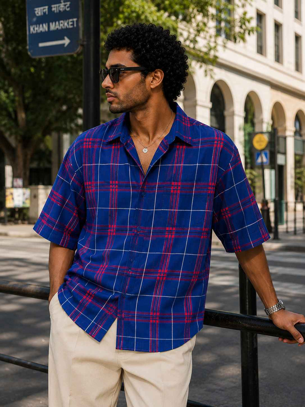 Man wearing a blue and red plaid shirt standing on a city street.