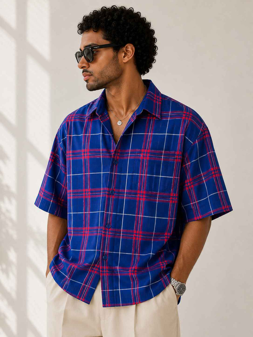 Man wearing a blue and red plaid shirt with sunglasses indoors.