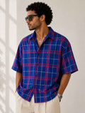 Man wearing a blue and red plaid shirt with sunglasses indoors.