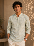 Man wearing a light green shirt standing against a textured wall.