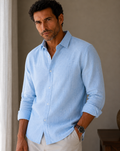 Man wearing a light blue shirt with rolled-up sleeves indoors.