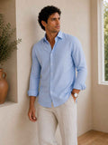 Man wearing a light blue shirt and beige pants standing indoors.