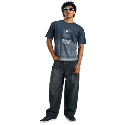 Person wearing a dark blue t-shirt with a graphic design and text, paired with dark jeans on a white background.