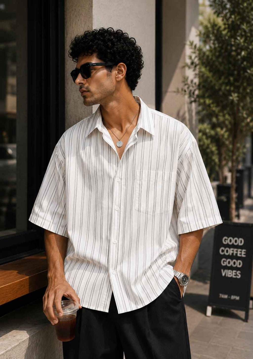 Man wearing a white striped shirt and sunglasses outdoors.