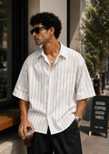 Man wearing a white striped shirt and sunglasses outdoors.