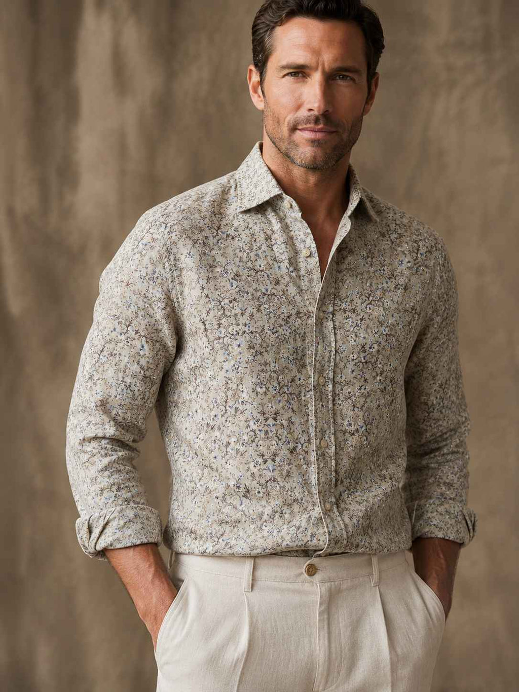 Man wearing a patterned shirt and light pants against a neutral background