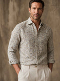 Man wearing a patterned shirt and light pants against a neutral background