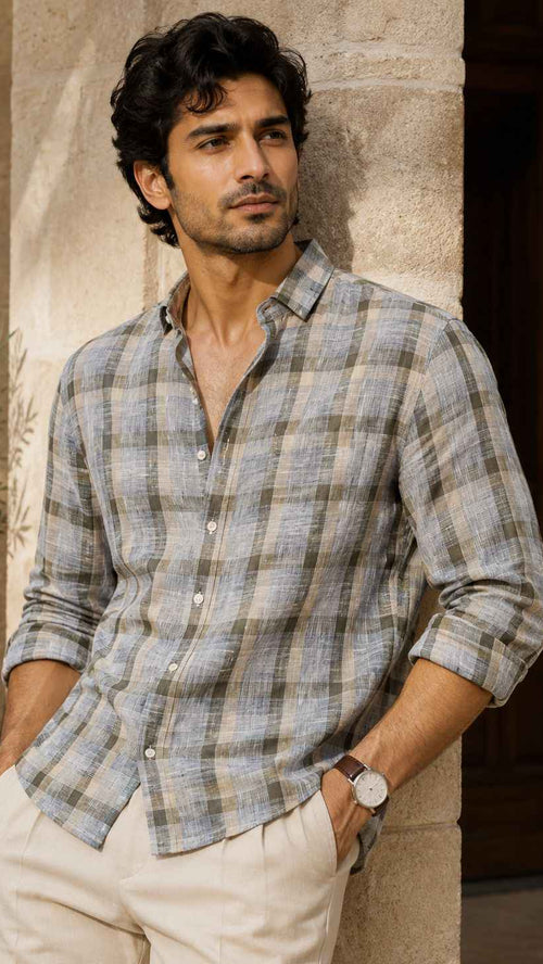Man wearing a checkered shirt standing against a stone wall with a plant in the background