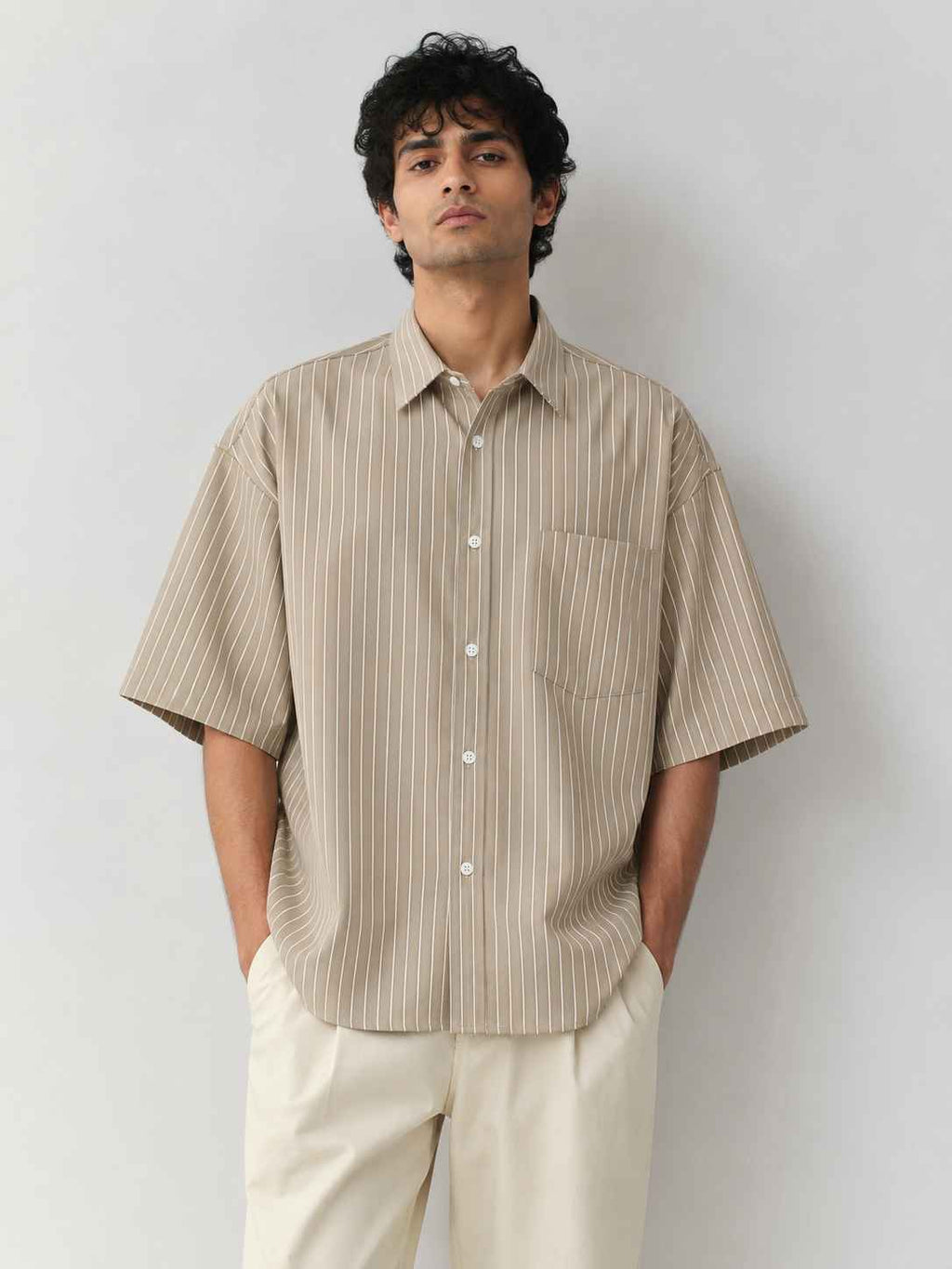 Man wearing a beige striped shirt and white pants against a plain background