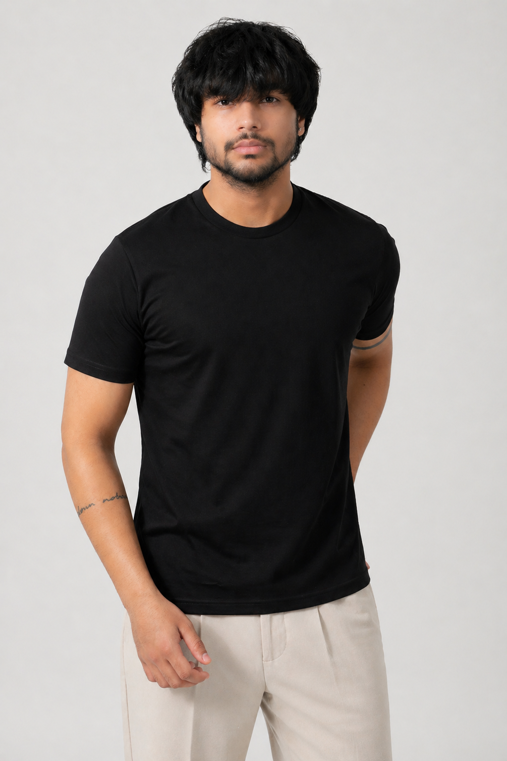 Man wearing a black t-shirt and light-colored pants on a plain background