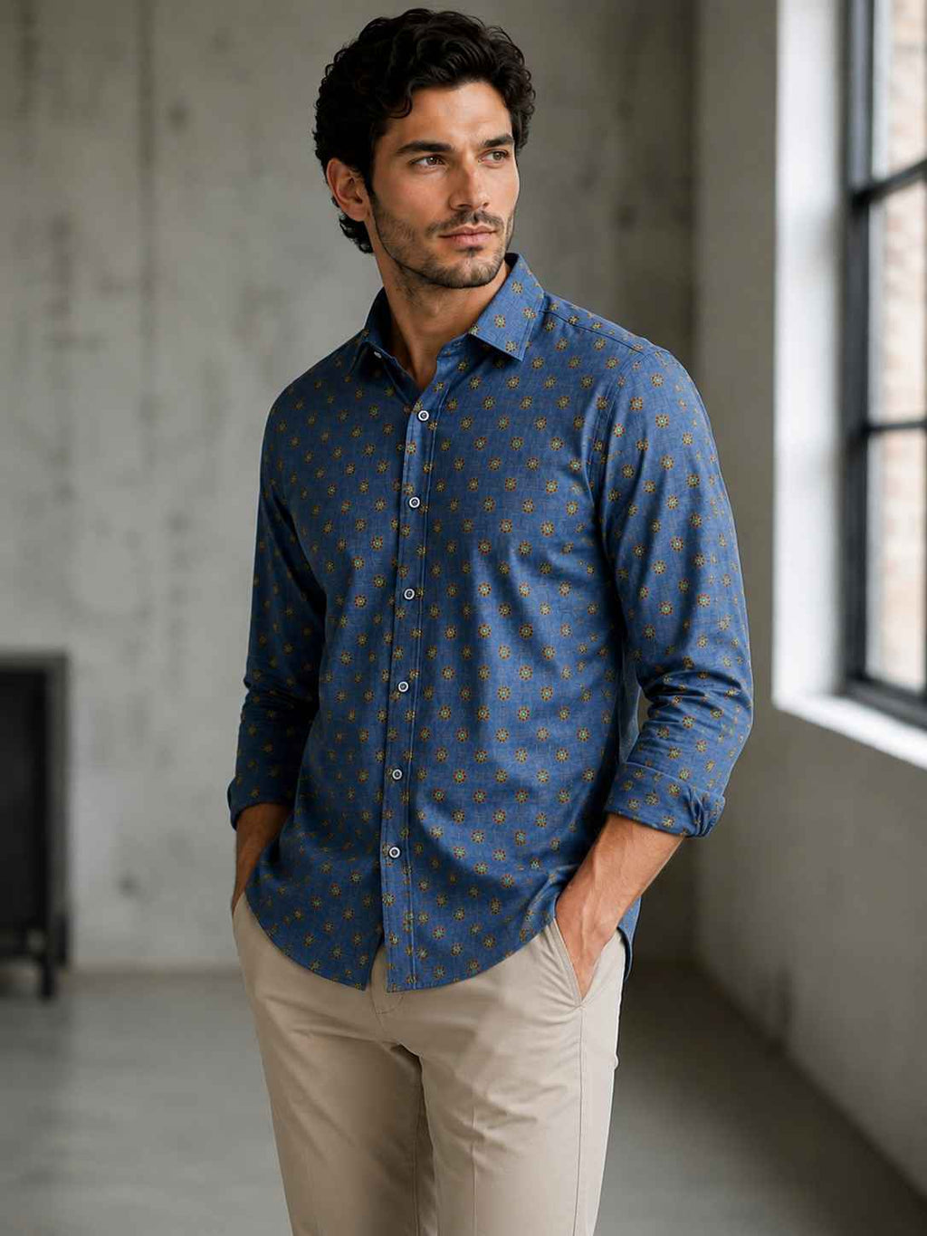 Man wearing a blue patterned shirt and beige pants in an indoor setting.