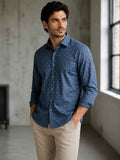 Man wearing a blue patterned shirt and beige pants in an indoor setting.