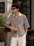 Man in a striped shirt and sunglasses holding a drink outdoors.