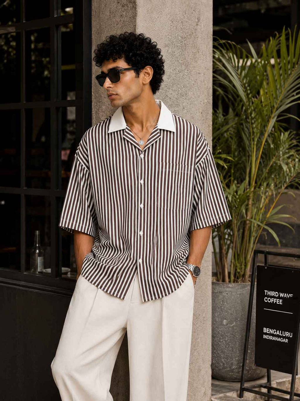 Man wearing a striped shirt and sunglasses standing outdoors.