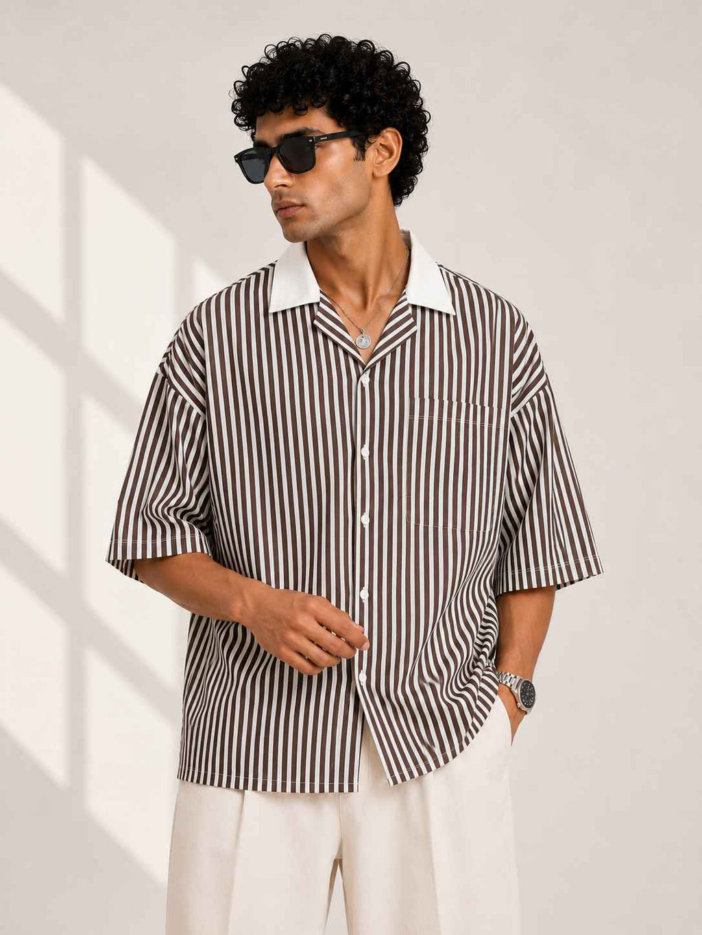 Man wearing a brown and white striped shirt with sunglasses indoors.