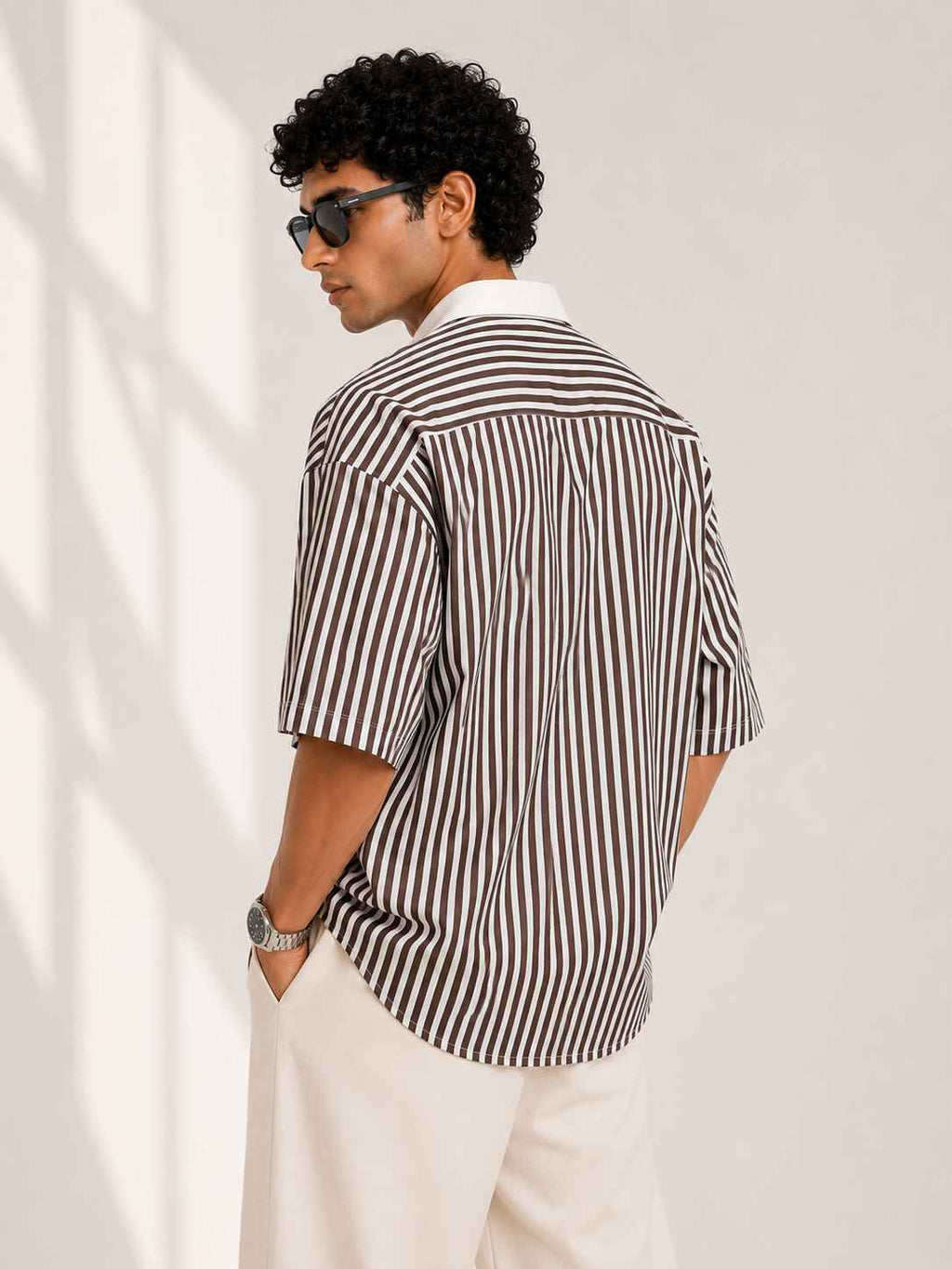 Man wearing a black and white striped shirt and sunglasses against a plain background