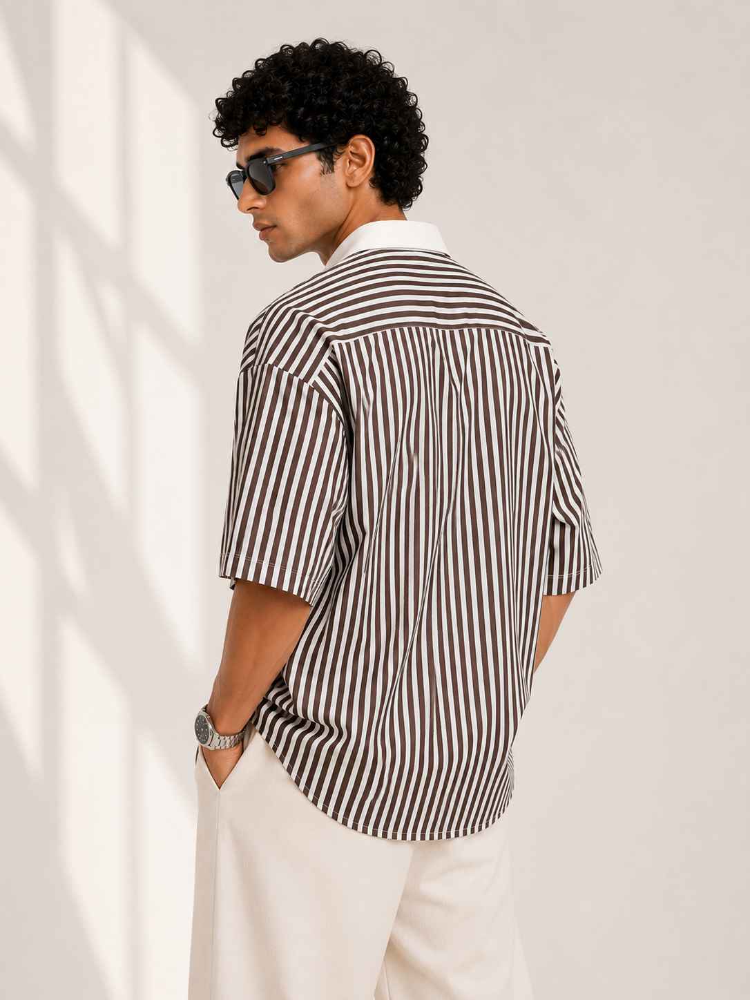 Man wearing a black and white striped shirt and sunglasses against a plain background