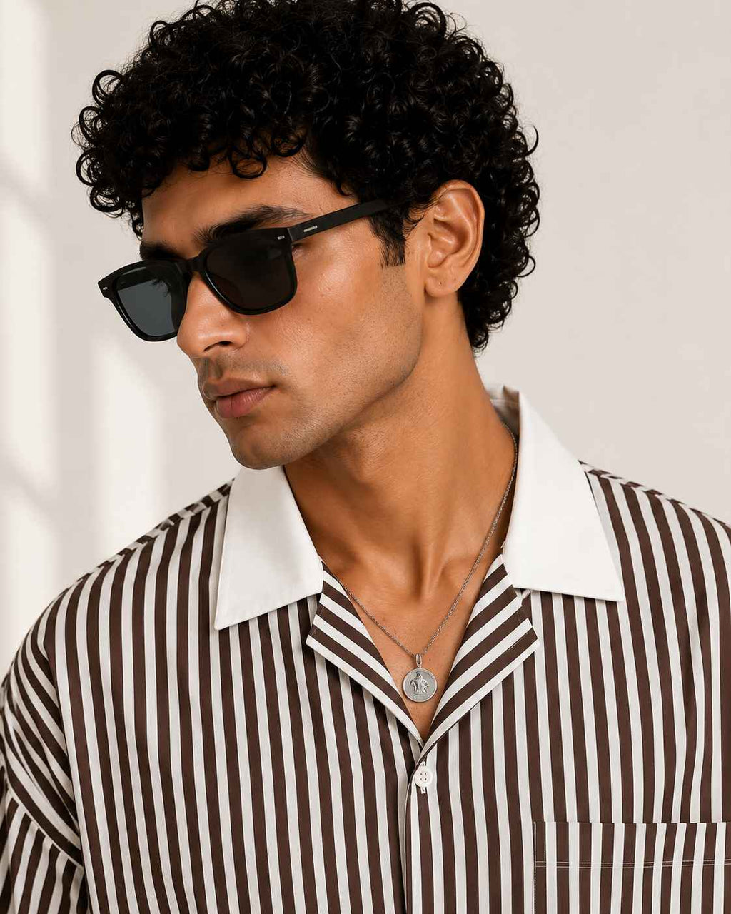 Man wearing sunglasses and a striped shirt against a plain background