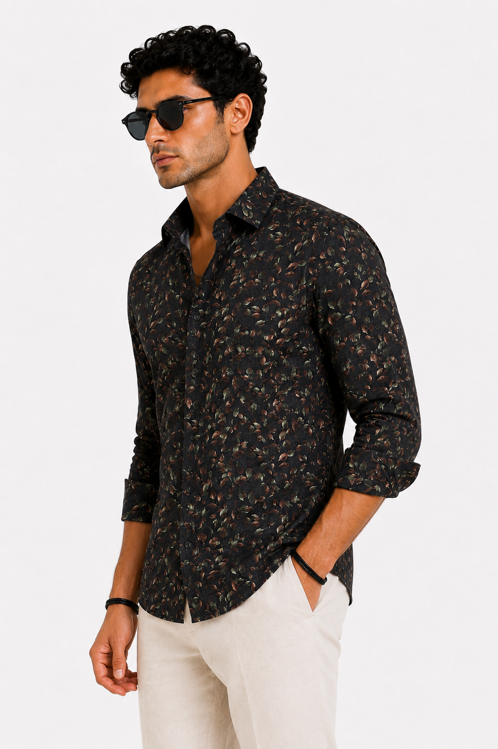 Man wearing a dark patterned shirt and white pants on a light gray background