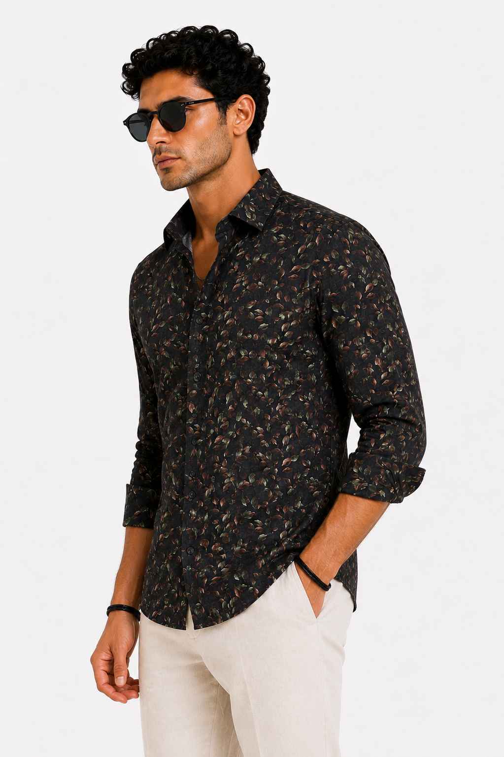 Man wearing a dark patterned shirt and white pants on a light gray background
