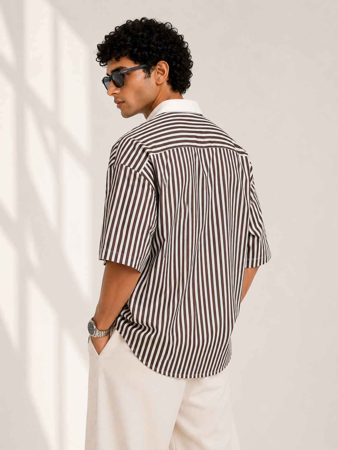 Man wearing a dark brown and white striped shirt and sunglasses against a plain background