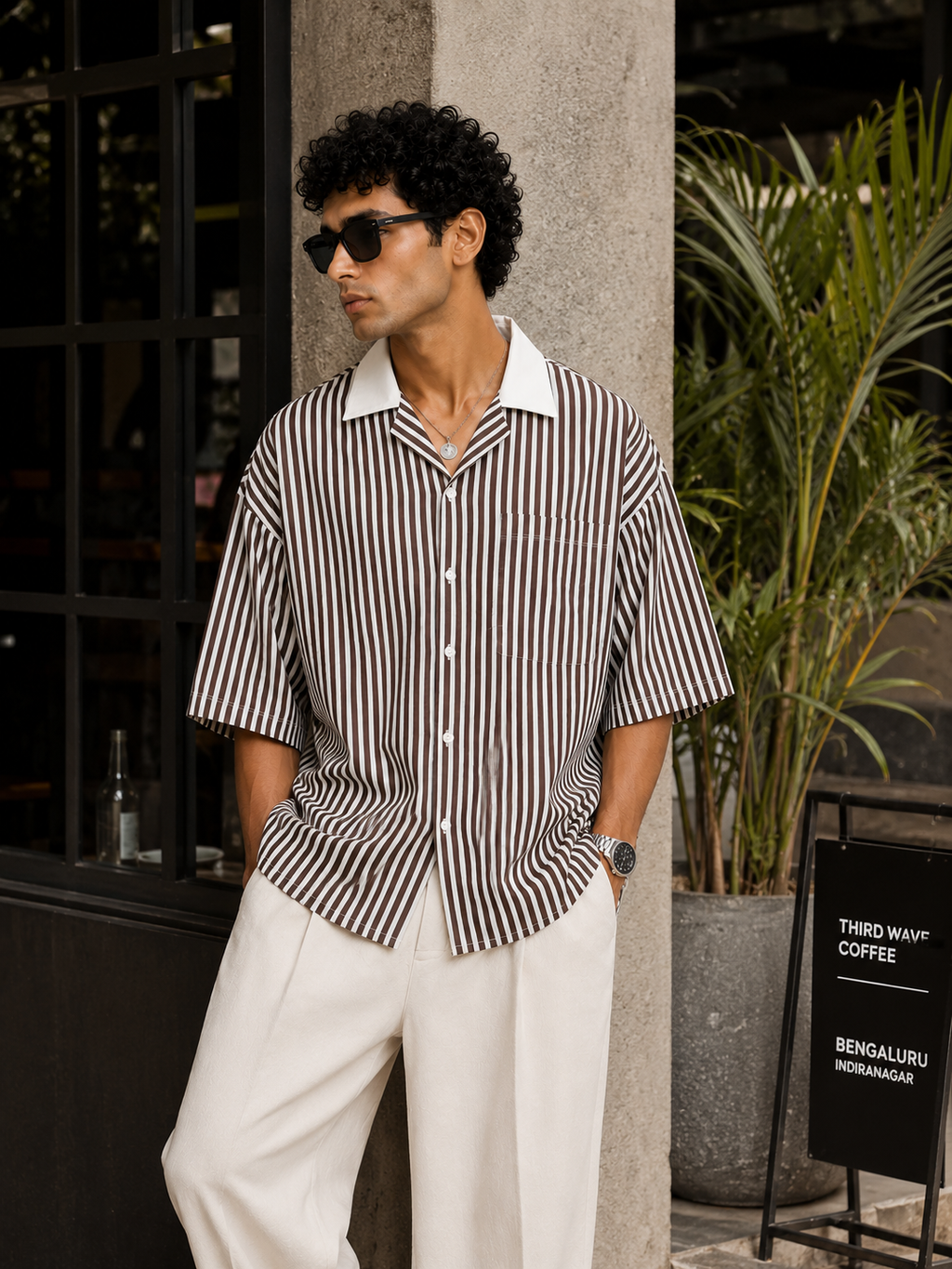 Man wearing a striped shirt and sunglasses standing outdoors near a building.
